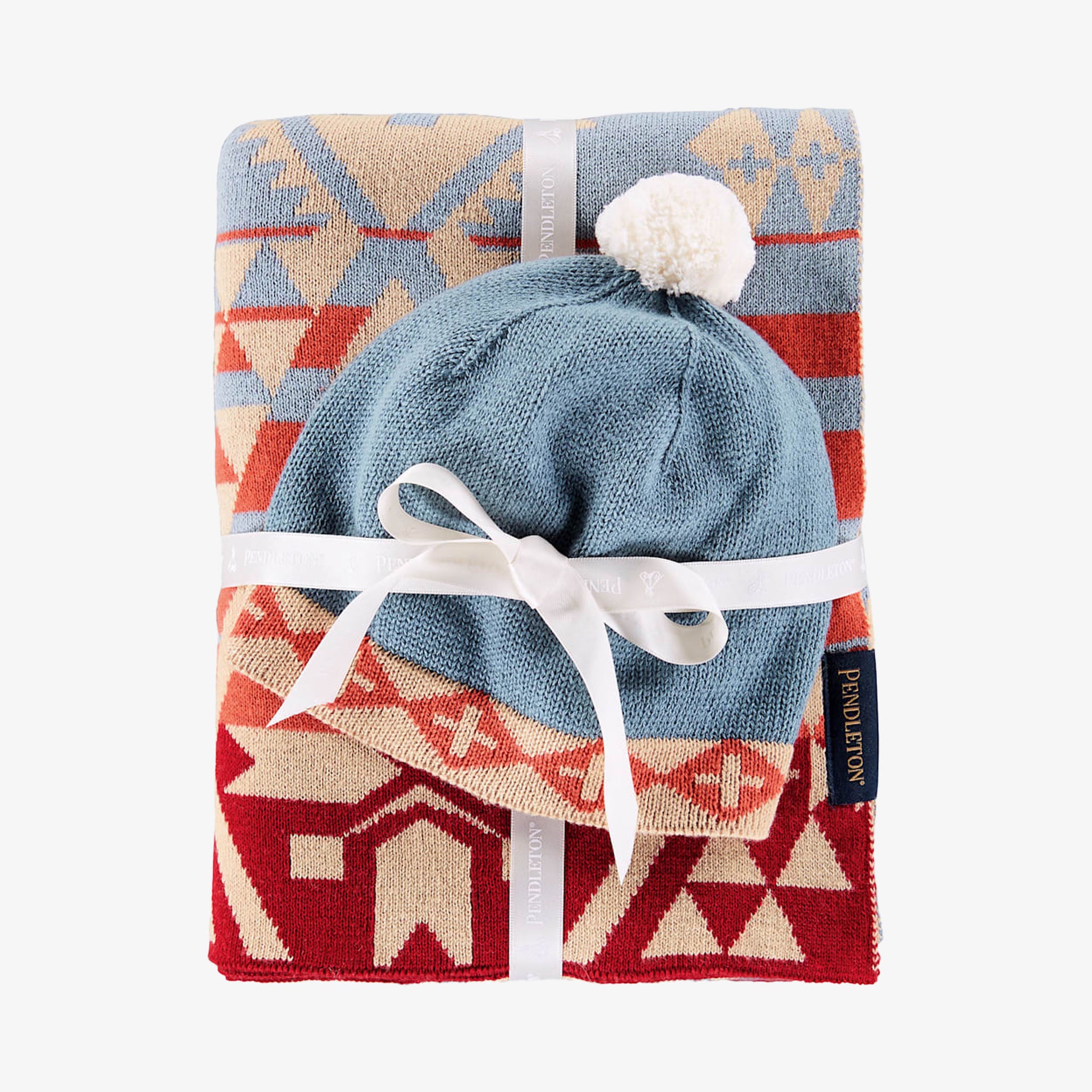 Blue baby hat with white pom-pom on a patterned blanket