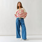 Woman wearing Aaron & Amber Lace Up red and white striped sweater with blue jeans on a white background
