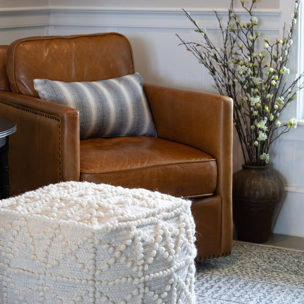 Leather chair with white pouf in front and Rustic brown jar like vase with embossed pattern beside chair