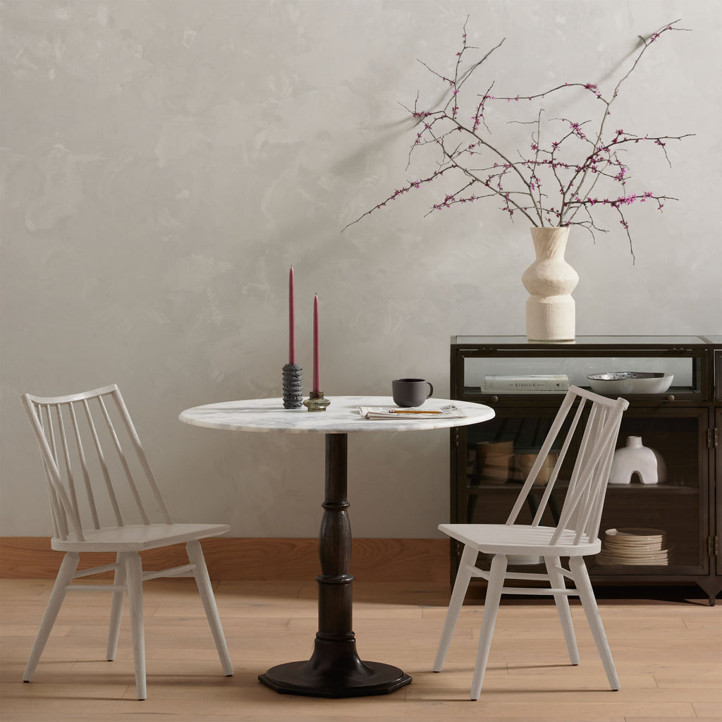 Four Hands Lewis Windsor Chair pair in Off White  around a pedestal dining table in a moody space