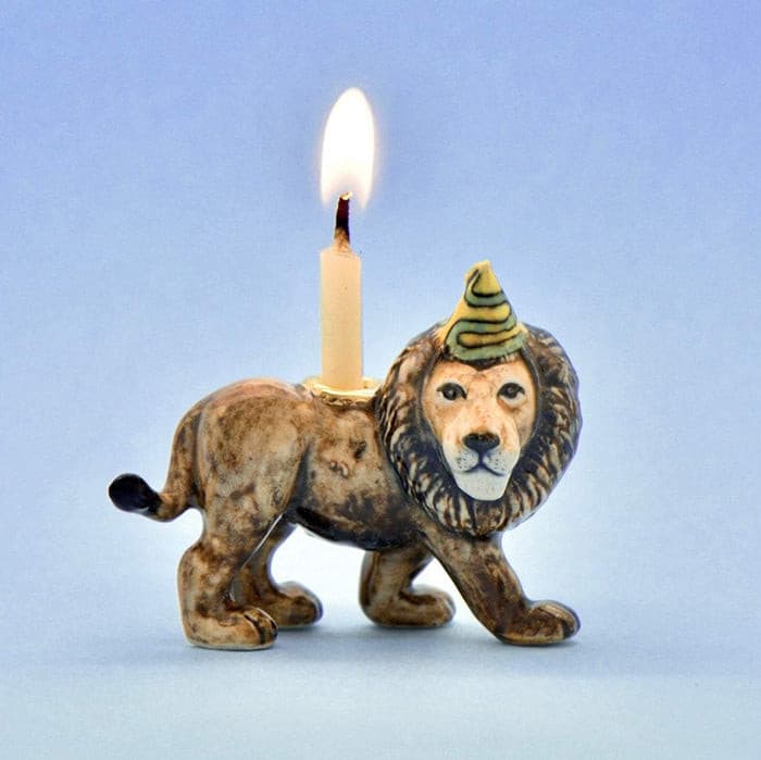 Lion-shaped candle holder with a lit candle on a light blue background