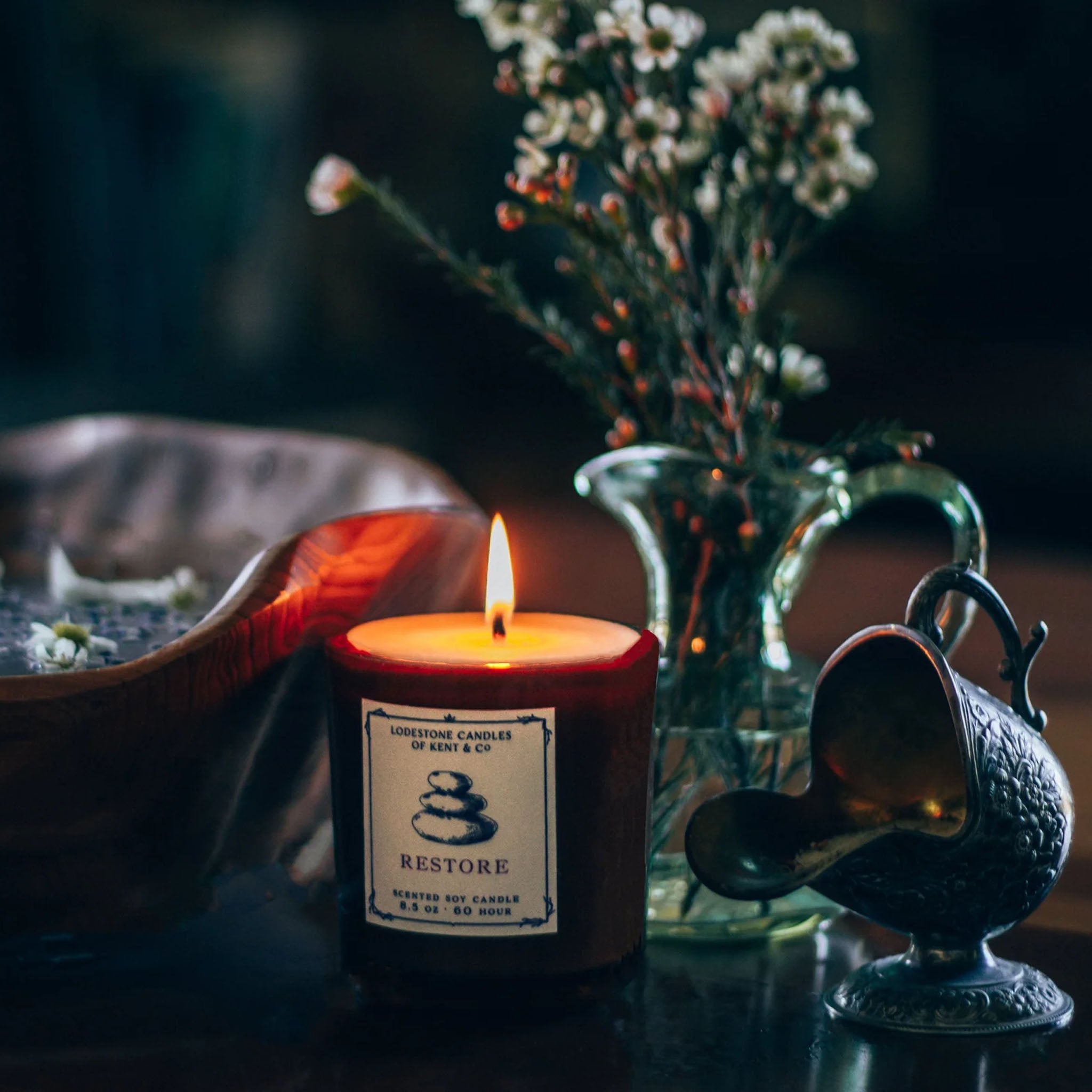 Lodestone Restore Candle on a table with a vase and a metal urn 