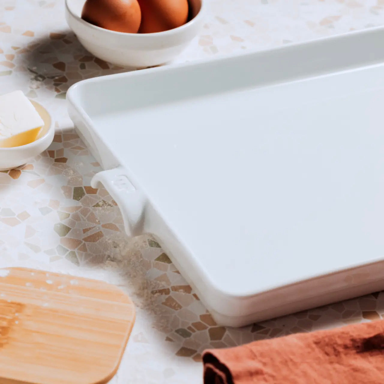 White baking dish on a kitchen counter with eggs and butter nearby