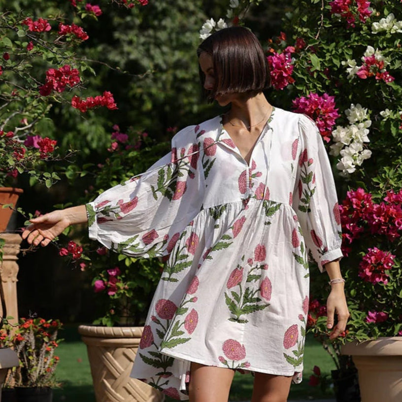 Model wearing Maison Marigold Taj Mini Dress in Pink on stone steps with flowering plants in the background