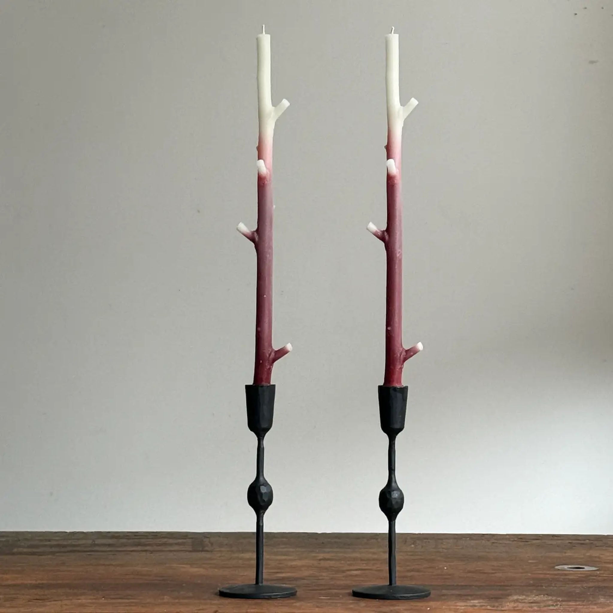 Two candle holders made from branches with black bases on a wooden surface.