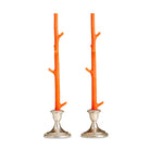 Two orange branch-like candle holders with silver bases on a white background