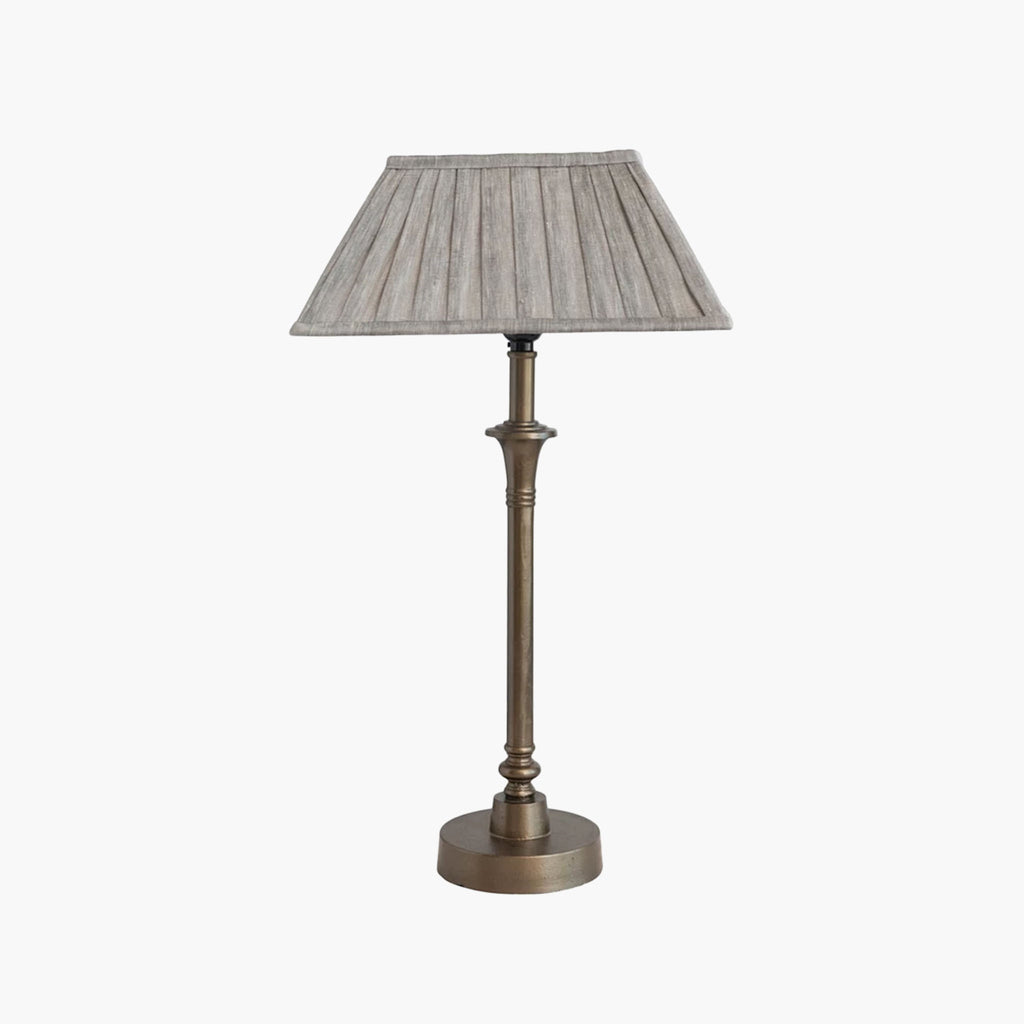 Metal candlestick style lamp with aged brass finish and rectangular linen shade on a white background