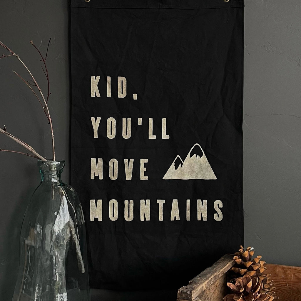 Black flag hanging on a wall with words 'kid you'll move mountains' saying on it