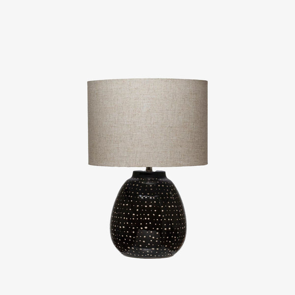 Round lamp with black base with white accent dots and a linen shade on a white background