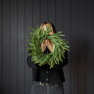 Norfolk & Cypress Mixed Real Touch Mini Wreath, 12" being held in front of a black wall at Addison West