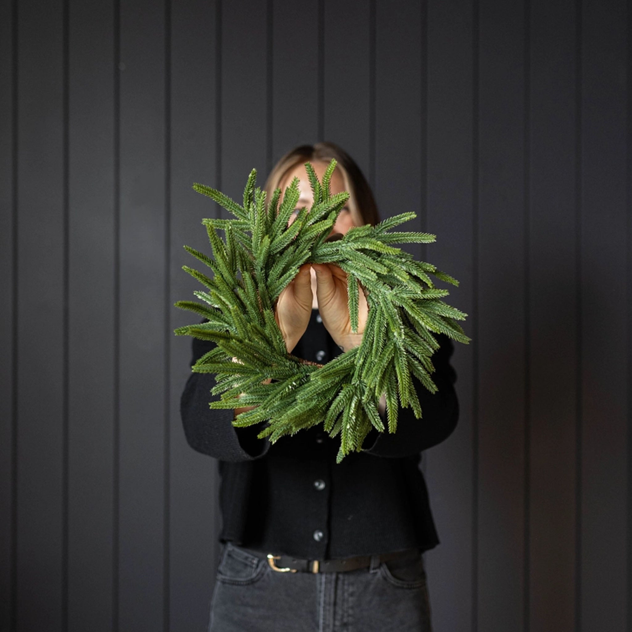 Norfolk & Cypress Mixed Real Touch Mini Wreath, 12" being held in front of a black wall at Addison West