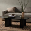 Four Hands Paden Coffee Table in Aged Black Acacia in a dimly lit living space with grey sofa