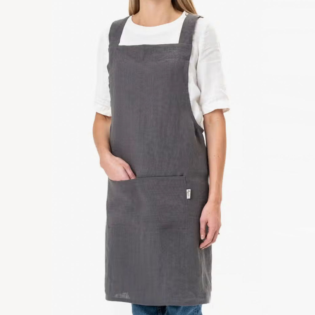 Female model wearing white tshirt and jeans with grey Pinafore Cross-Back Linen Apron in Charcoal Grey