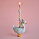 Decorative goose holding a colorful striped candle against a pink background