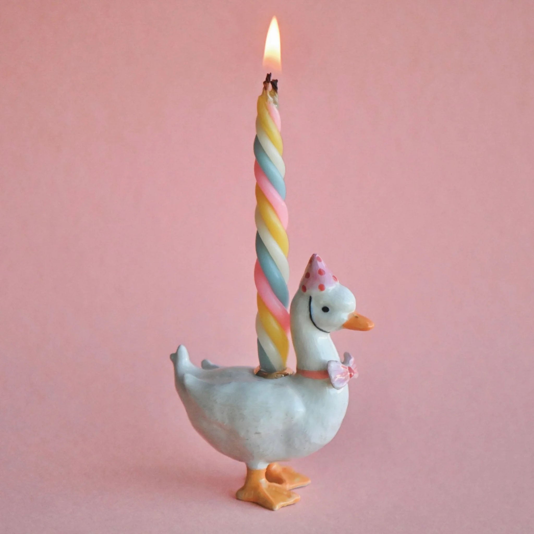 Decorative goose holding a colorful striped candle against a pink background