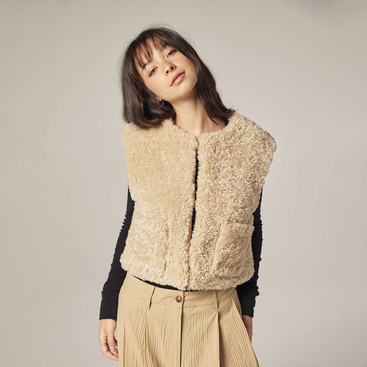 Woman wearing a beige sherpa vest against a plain background