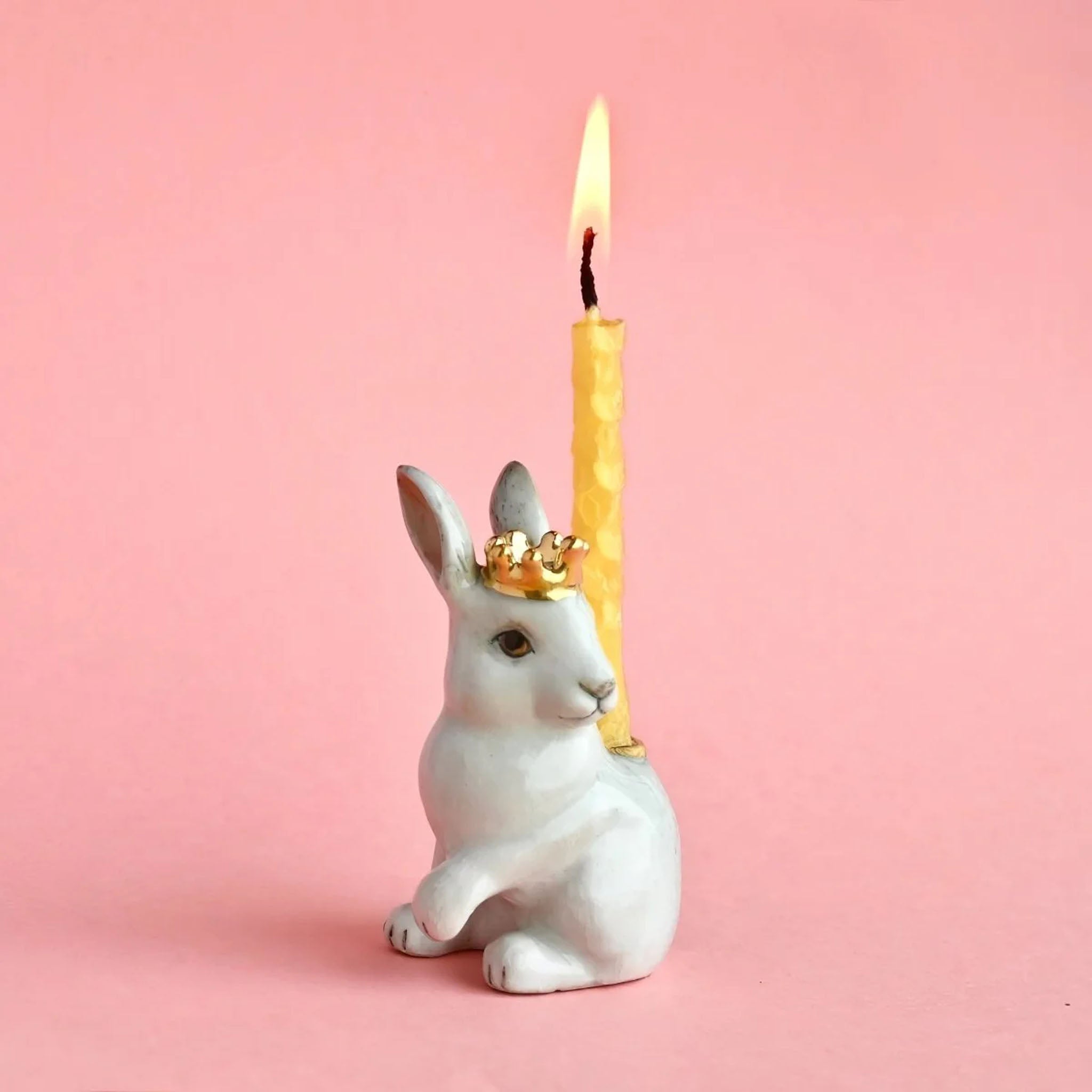 Ceramic rabbit-shaped candle holder with a lit yellow candle on a pink background