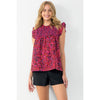 Blond model wearing THML Ruffle Sleeve Smocked Top in fuschia and purple in front of a white wall