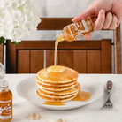 Hand pouring Runamok sparkle maple syrup over pancakes on a table with a white table cloth