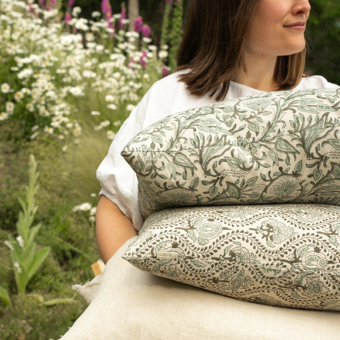 Person holding patterned pillows with a garden background