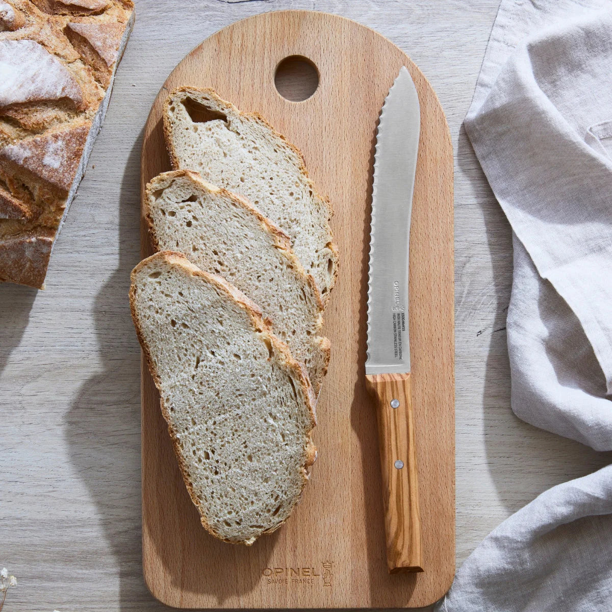 Sliced bread on a wooden cutting board with a knife, on a light wooden surface.