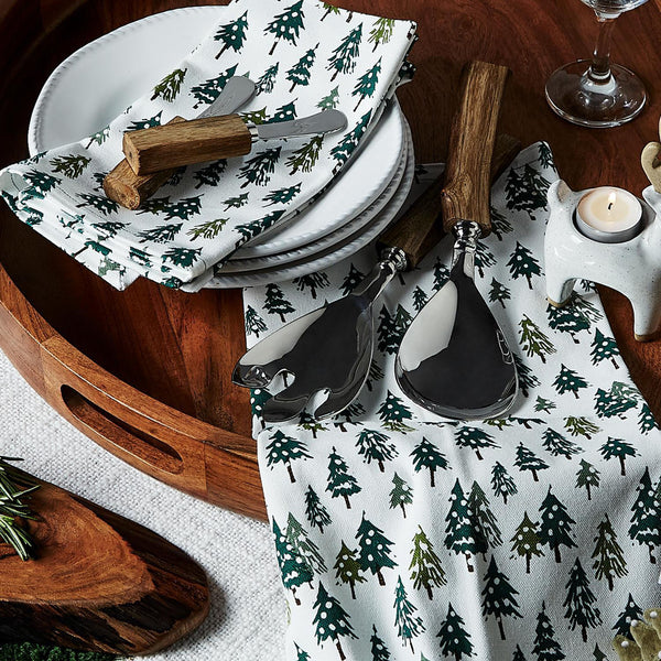 Wood tray with plates and serving utensils and white napkins with pine trees on them