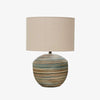 Stoneware lamp with muted stripes in browns and blues and linen shade on a white background
