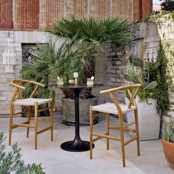Four Hands Simone Counter Table in Antique Rust with two chairs in an outdoor space with tropical plants