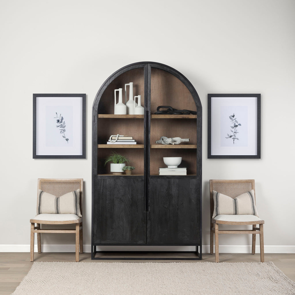 Arched top black wood cabinet with iron base and honey wood interior in a living space with two side chairs and decorative accessories