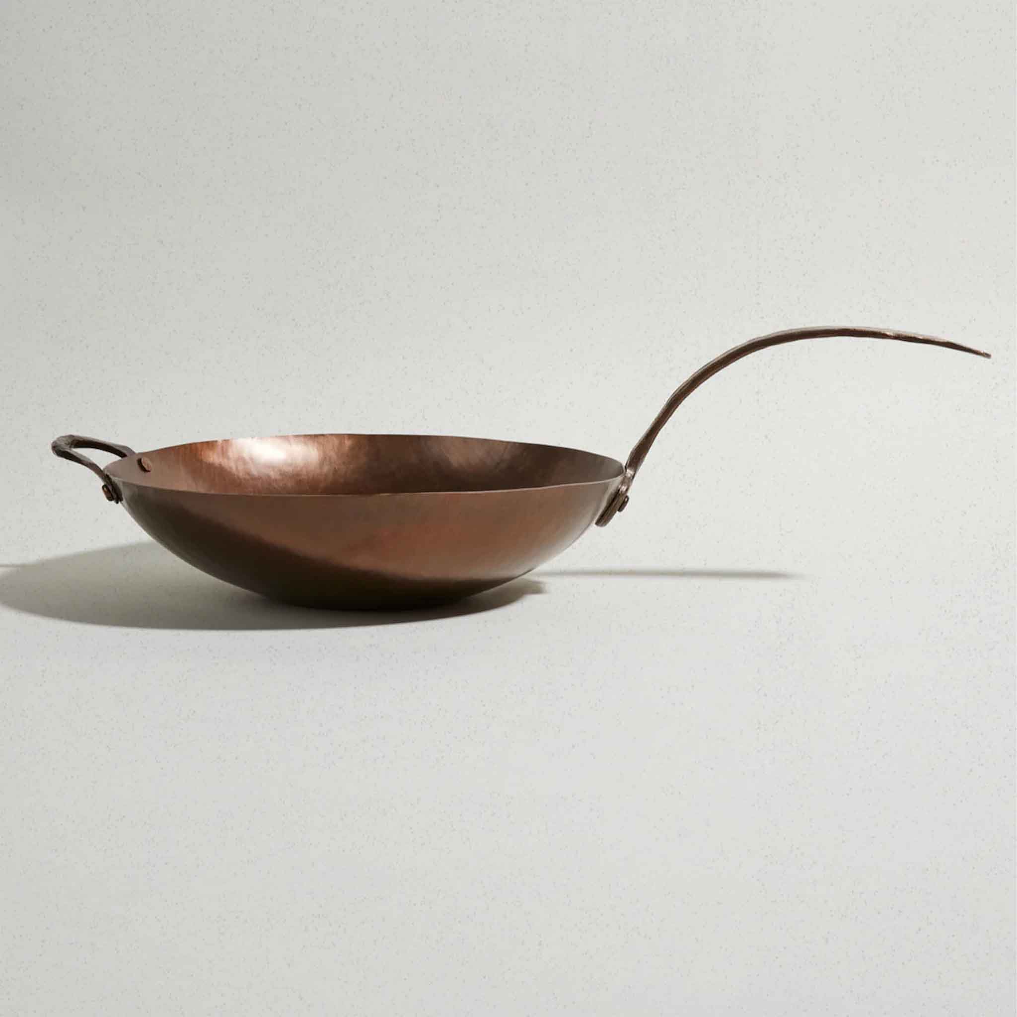 Profile view of Smithey carbon steel wok on a white background