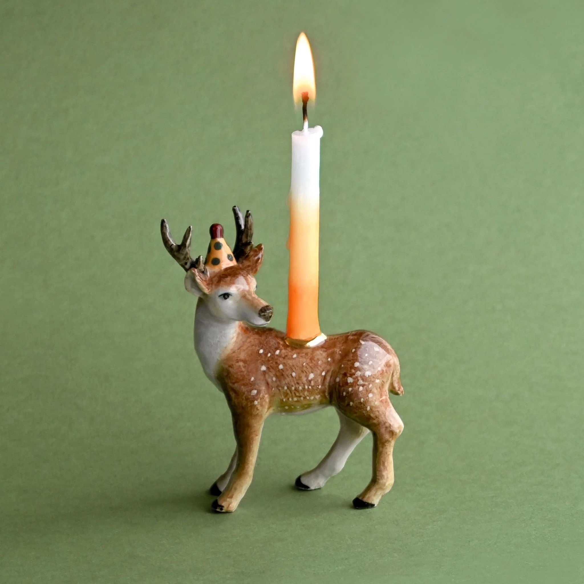 Deer-shaped candle holder with a lit candle on a green background