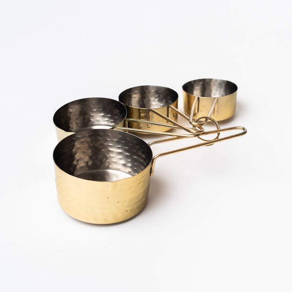 Set of four stainless measuring cups with brass toned finish on a white background
