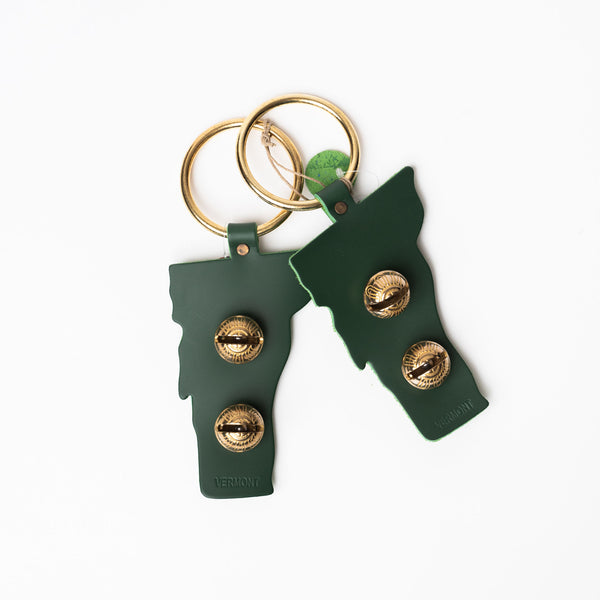 Bells for hanging on a door knob in green leather the shape of vermont with two bras bells on a white background