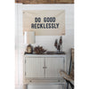 Small white side table with small metallic terracotta lamp flag above that says 'Do Good Recklessly'