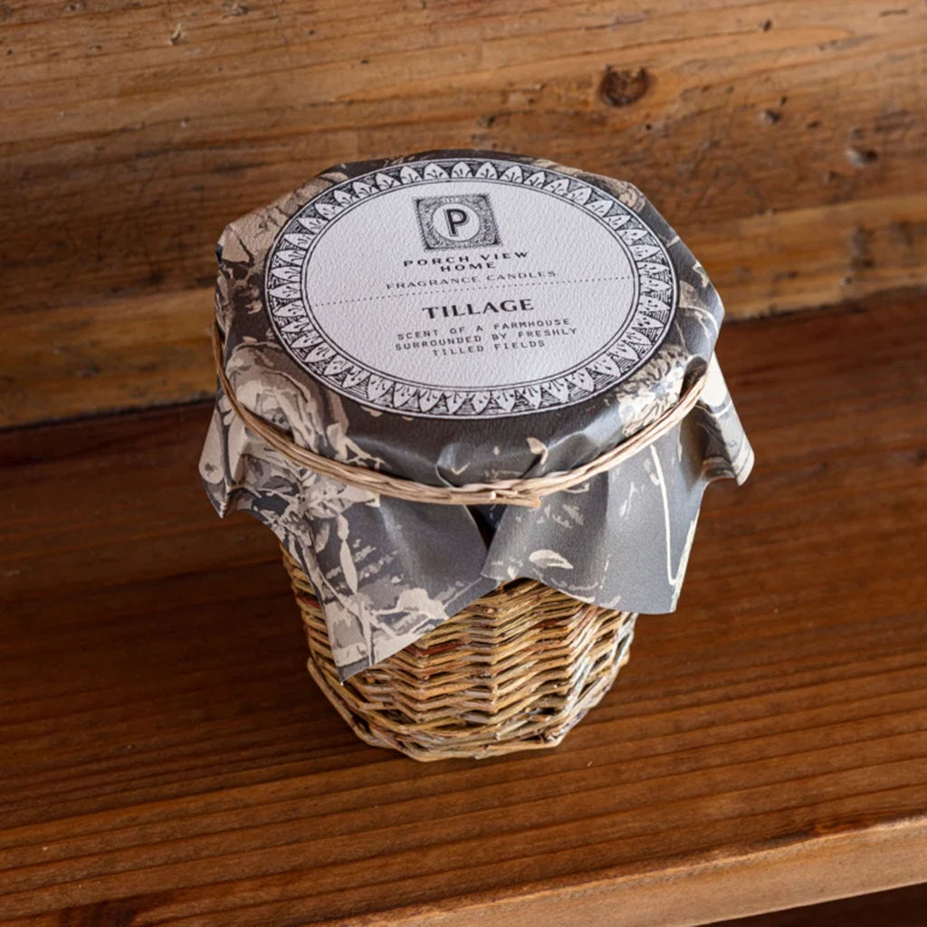 Porch View Home brand Tillage scented candle in willow wrapped vessel on a wood surface