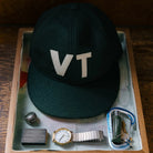 Warren Farm League Ballcap in Green Mountain State on a wood background at Addison West
