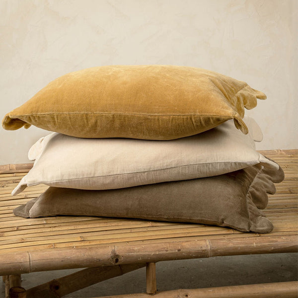 Stack of velvet pillows with scalloped edges on a bench in front of a beige wall 