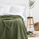 Green waffle weave bed blanket in a room with white walls and a white linen bed