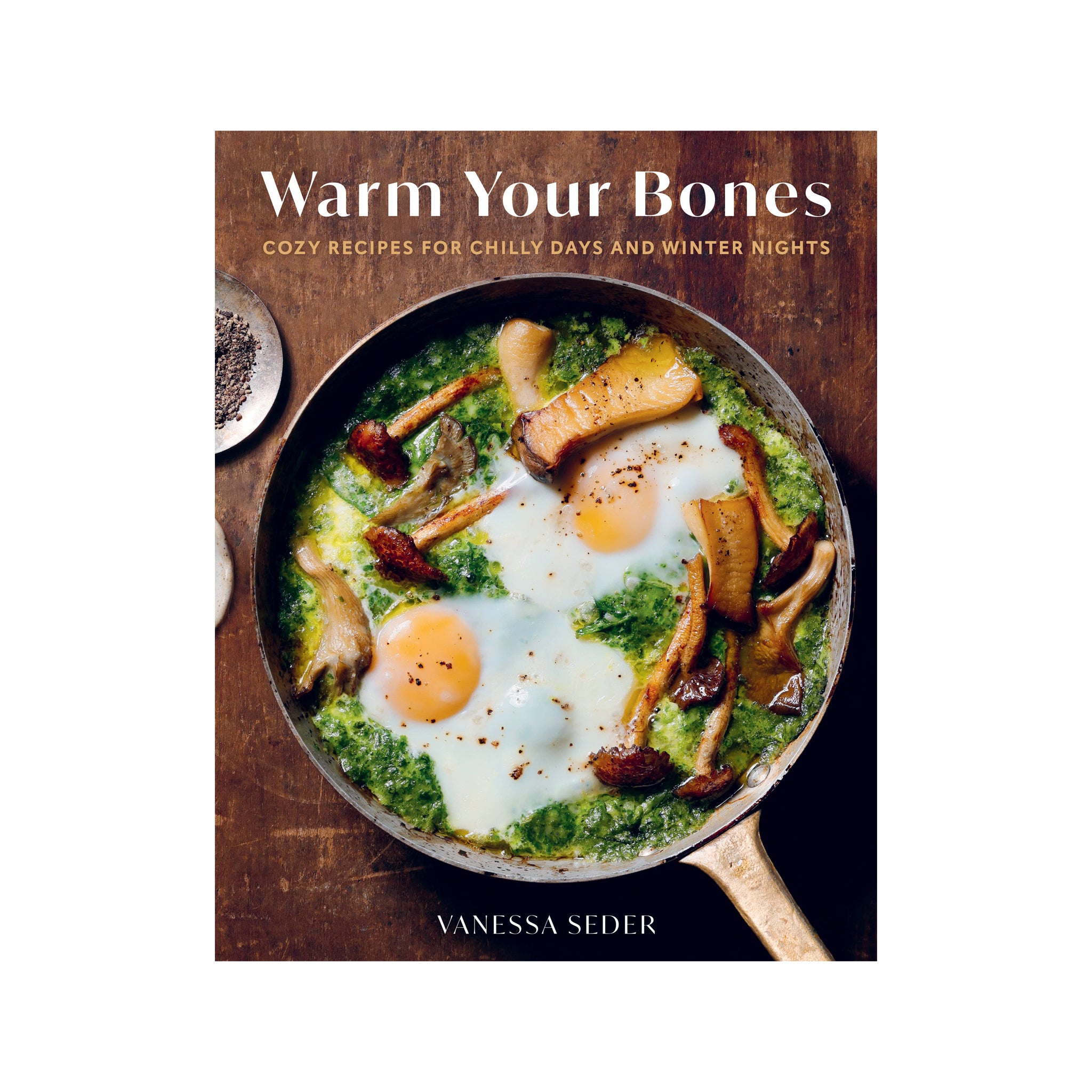 The front cover of the cookbook 'Warm Your Bones' by Vanessa Seder, featuring a top-down photograph of eggs in a skillet with mushrooms and green sauce on a rustic wooden background.