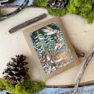 Woodland-themed card with animals and nature elements on a wooden surface with pinecones and branches.