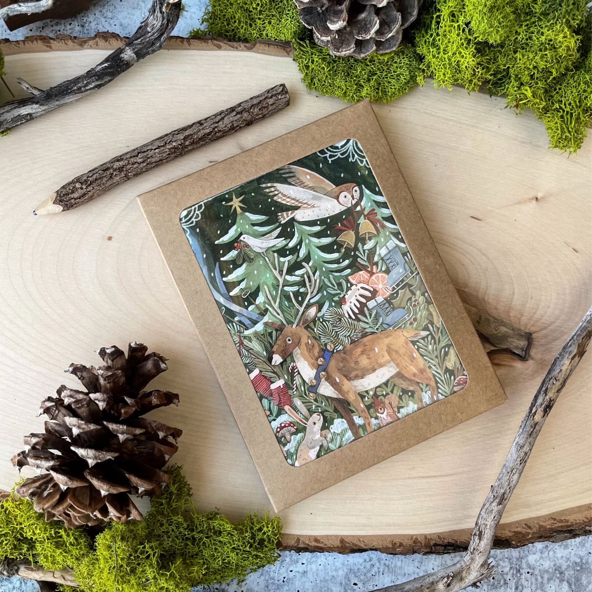 Woodland-themed card with animals and nature elements on a wooden surface with pinecones and branches.