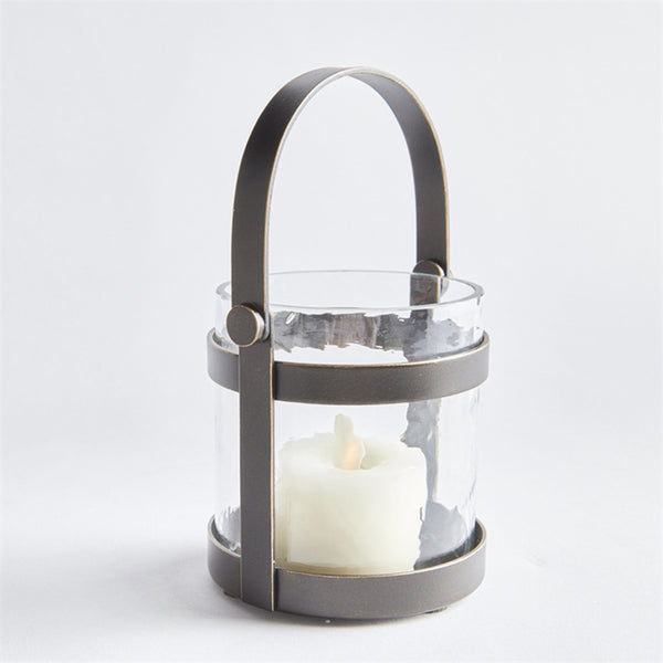 Glass candle holder with bronze strap detailing and handle for carrying on a white background