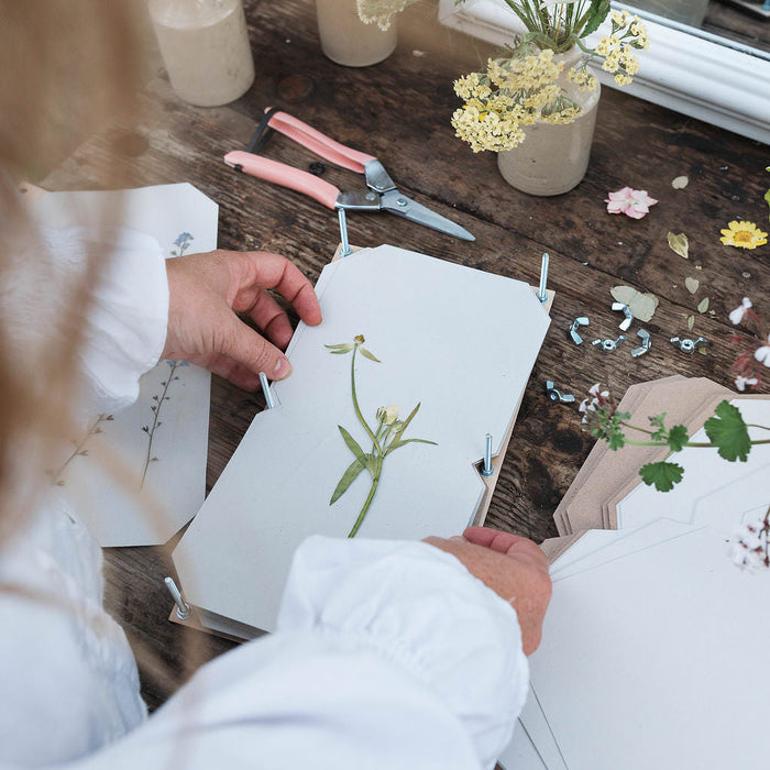 Person working with pressed flowers and tools on a wooden table