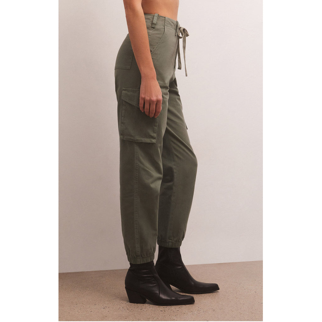 Model wearing black tank top and Z Supply Andi Twill Pant in Evergreen with black booties in front of a beige wall