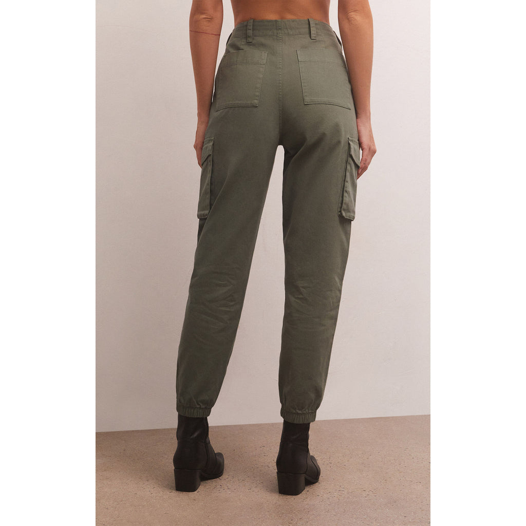 Model wearing Z Supply Andi Twill Pant in Evergreen with black booties in front of a beige wall