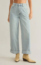 Model wearing Z Supply Lou Denim Pant in Faded Indigo with creme colored cowboy boots in front of a neutral backdrop
