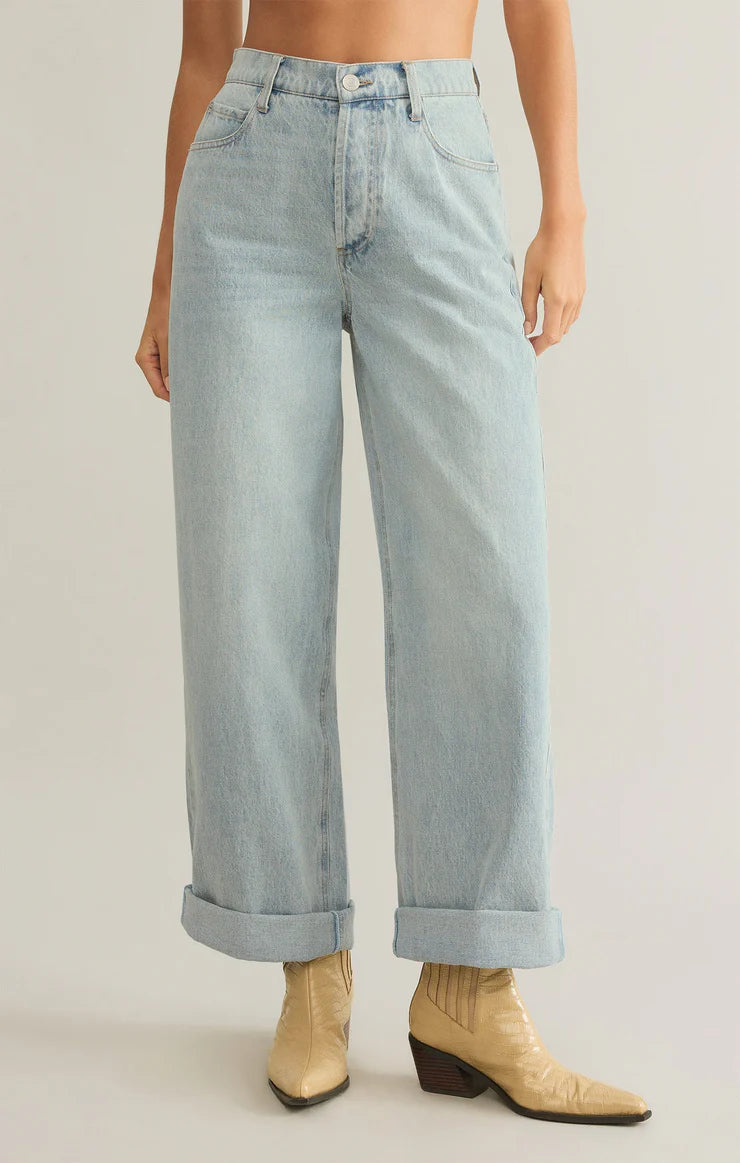 Model wearing Z Supply Lou Denim Pant in Faded Indigo with creme colored cowboy boots in front of a neutral backdrop