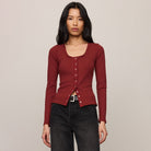 Woman wearing a red cardigan and dark jeans against a plain background