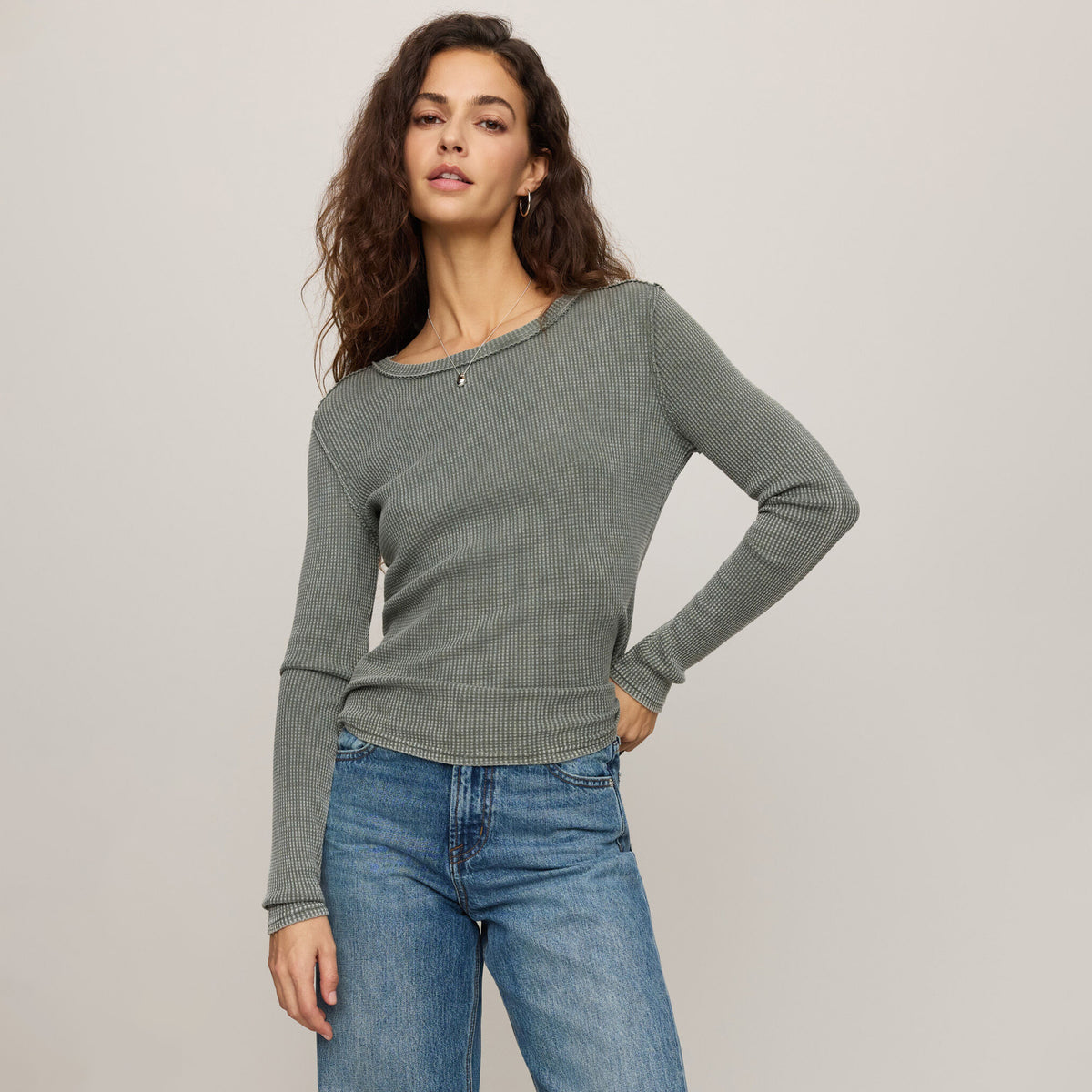 Woman wearing a gray sweater and blue jeans on a plain background