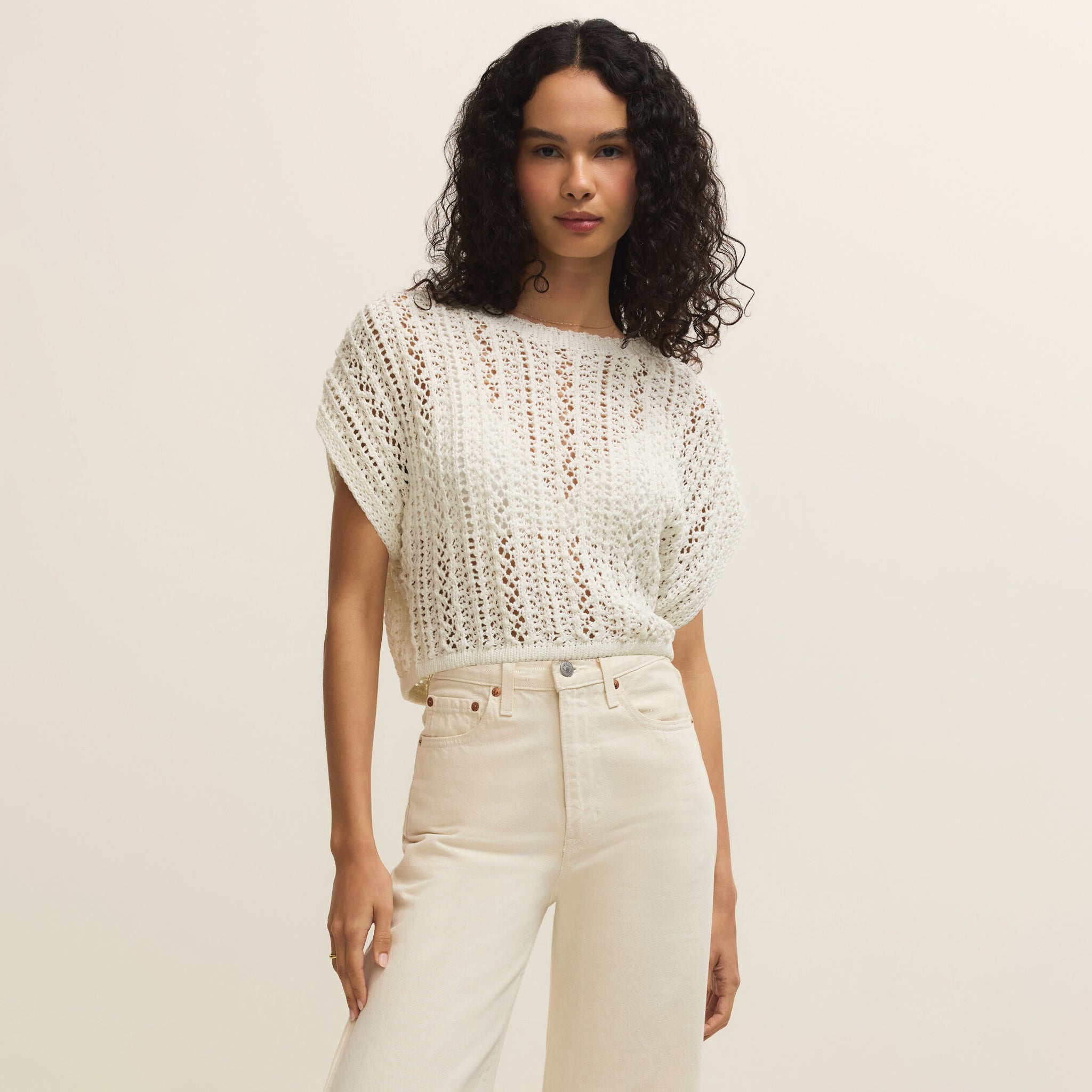 Woman wearing a white crochet top and beige pants on a plain background
